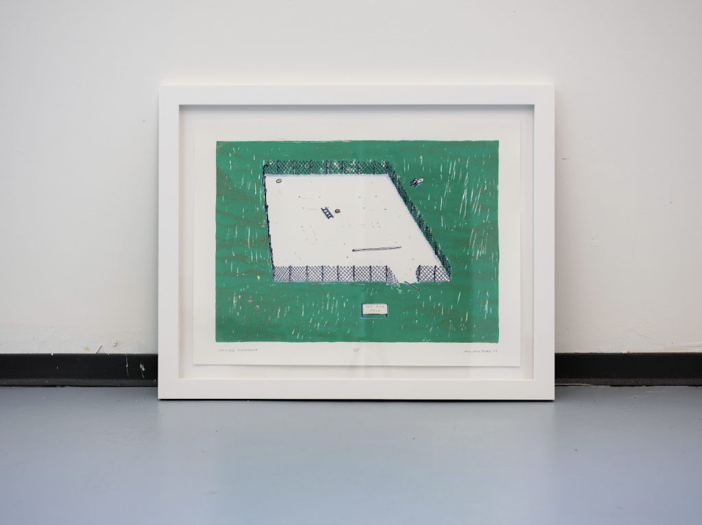 A framed print is propped against a wall and sits on the gray studio floor. The print depicts a fenced playground in a green field with a section of the fence broken near the right side of the image and a collection of objects, including a ladder, several sticks, and a "Lot for Sale" sign dot the empty playground. 